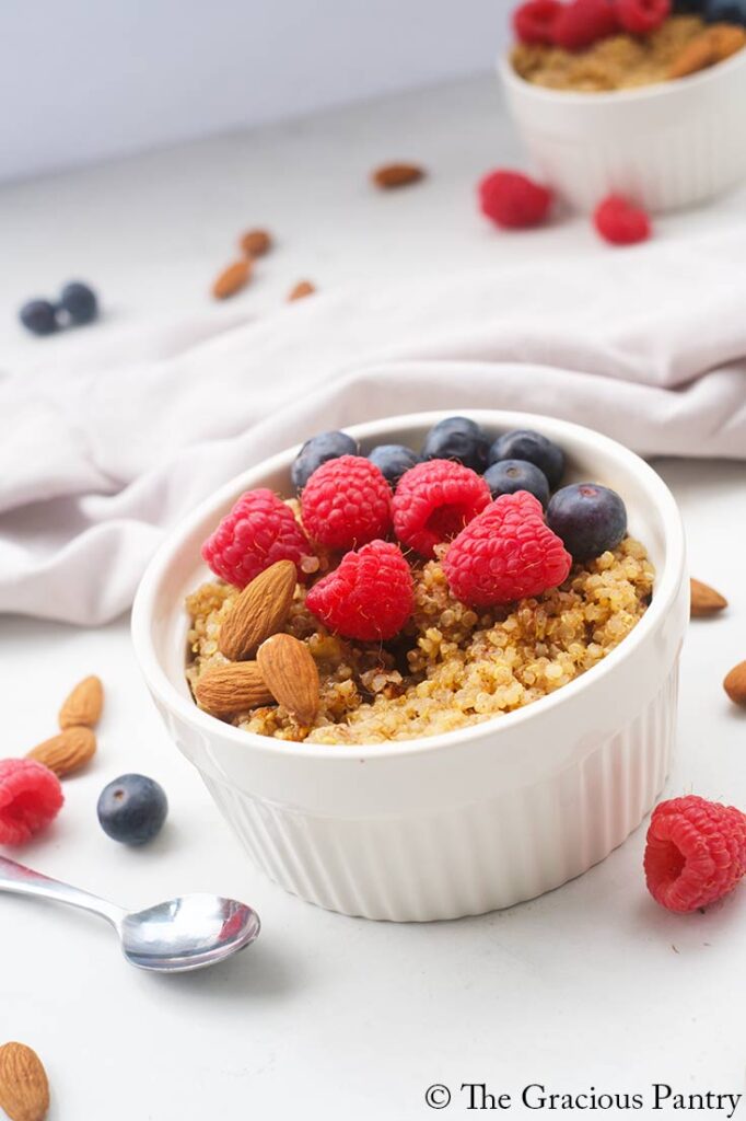 An angled view of a white bowl filled with Breakfast Quinoa which is topped with fresh berries.