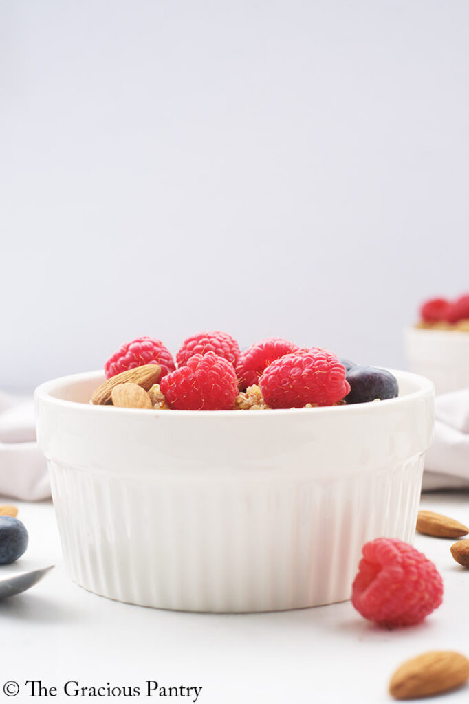 A side view of a white bowl filled with Breakfast Quinoa. Fresh raspberries and blueberries are visible just over the rim.