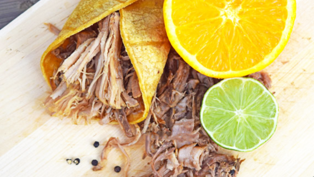 An overhead view of some shredded pork on a cutting board, both on the board and inside a corn tortilla.