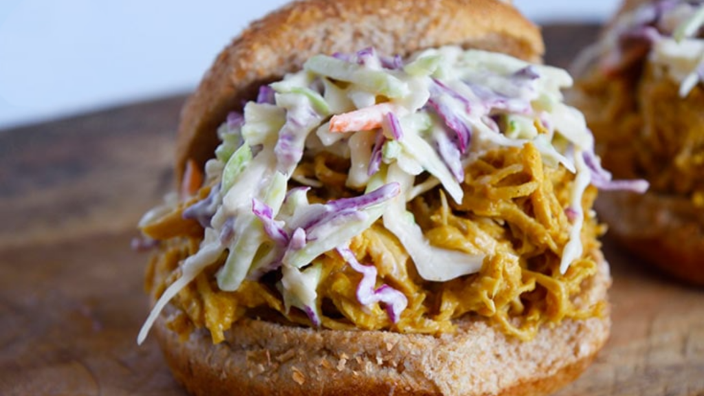 A closeup of a Carolina Gold BBQ Chicken sandwich topped with creamy coleslaw on a whole grain bun.