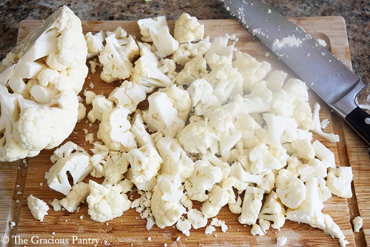 Chopped cauliflower laying on a wood cutting board.