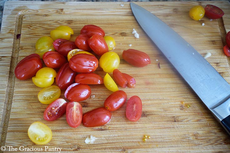 Halved grape tomatoes on a wood cutting board.