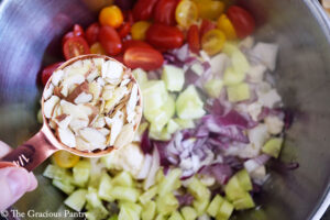 Adding sliced almonds to the cauliflower salad in a large mixing bowl.