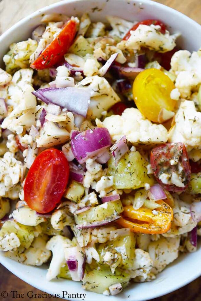 An overhead closeup of a white bowl filled with cauliflower salad.