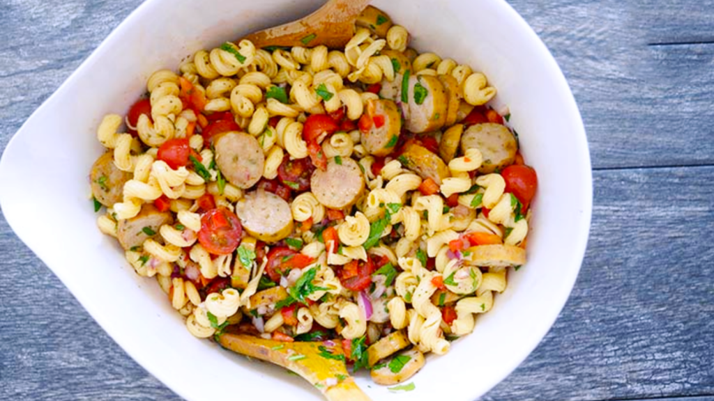 An overhead view of a white mixing bowl filled with cavatappi pasta salad.