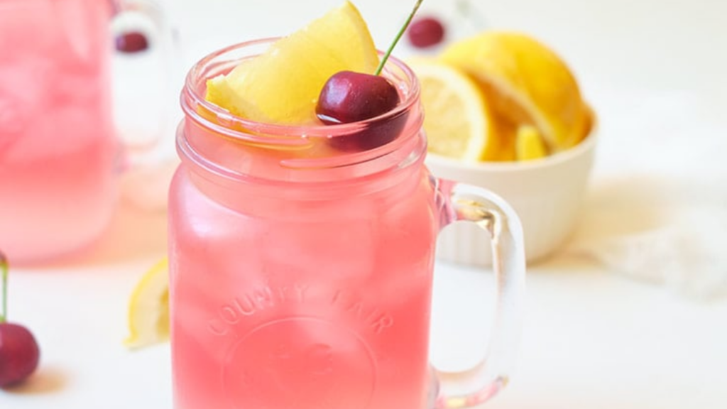 An up close view of a glass mug filled with cherry green tea lemonade and garnished with a lemon wedge and fresh cherry.