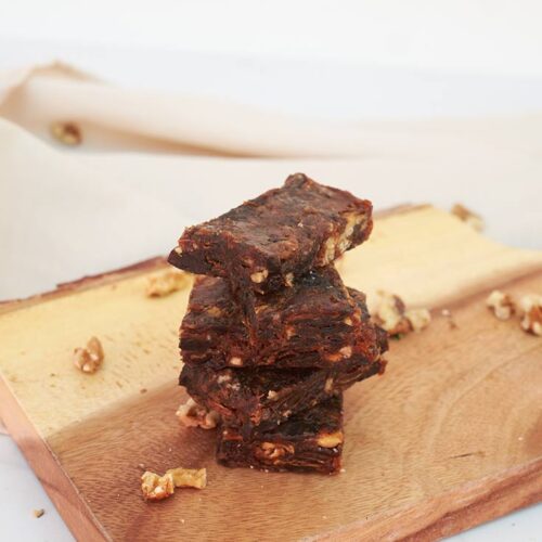 A stack of Cherry Pie Lara Bars sit on a wood cutting board with nut pieces sprinkled around them.