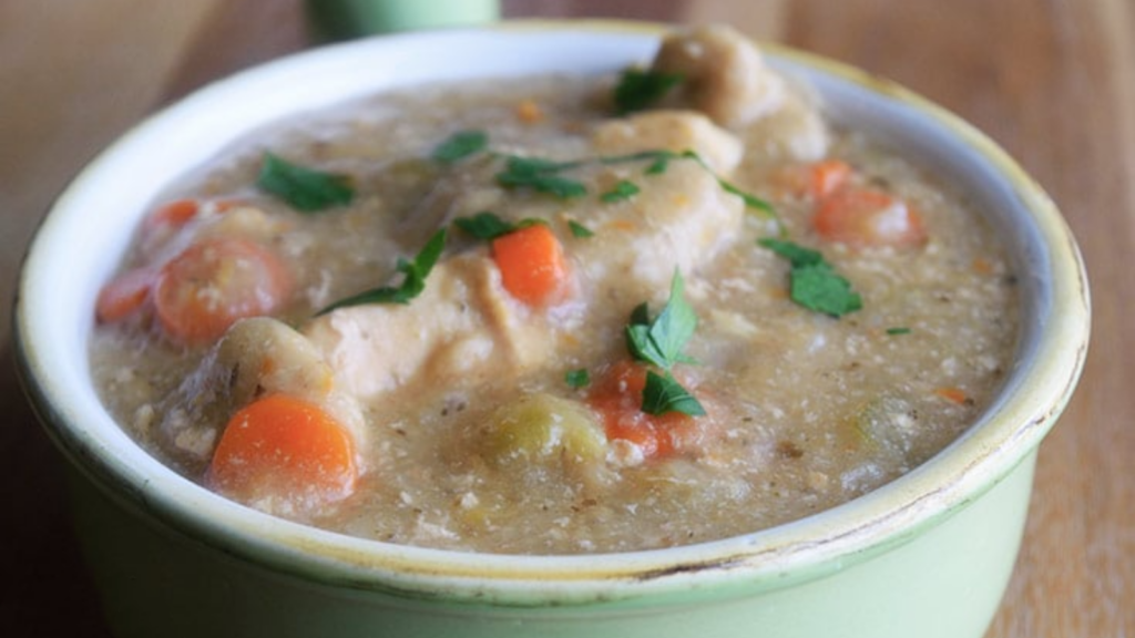 A light green crock sits filled with healthy chicken and dumplings.
