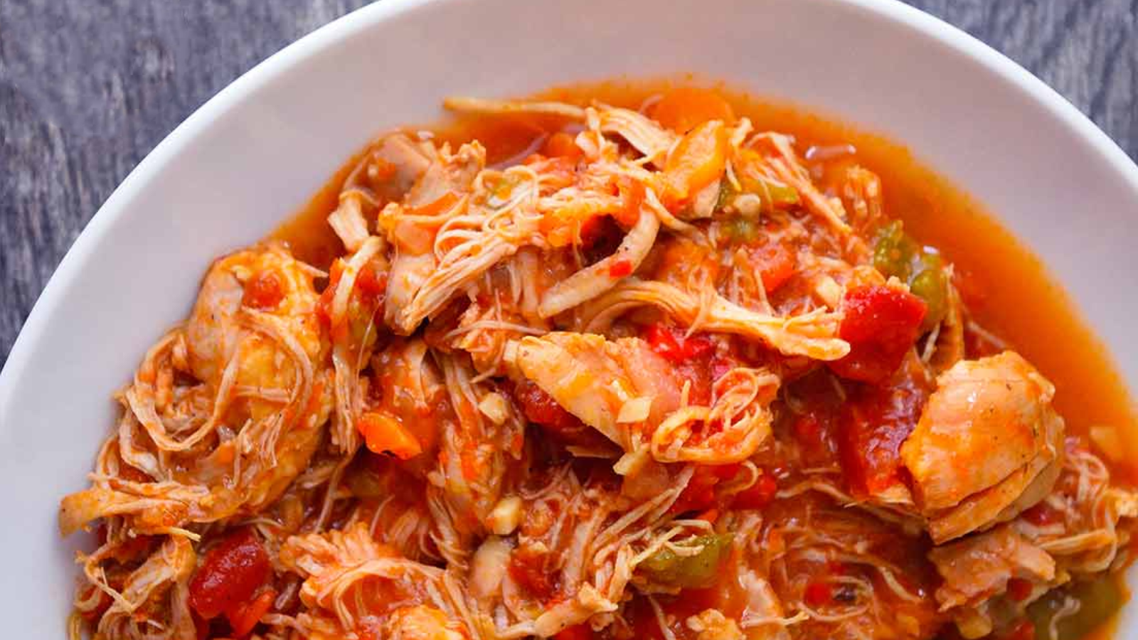 A partial view of a white bowl filled with chicken ropa vieja.