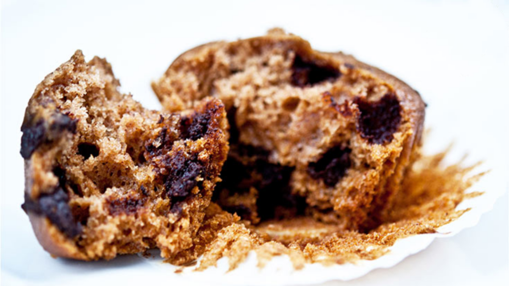 A chocolate chip muffin broken in half and laying on a white surface.