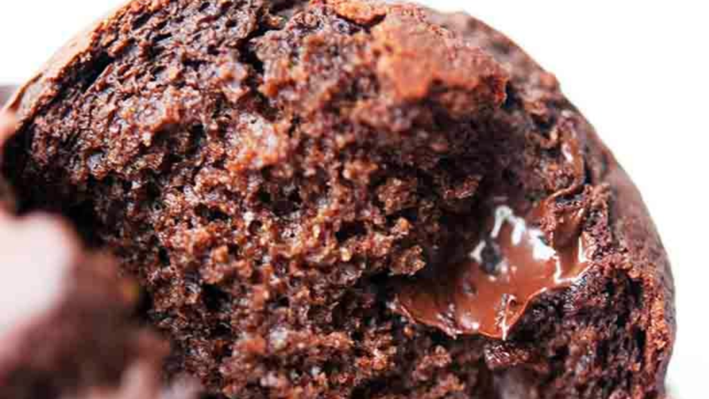 A single chocolate chocolate chip muffin broken open to show a melting chocolate chip.
