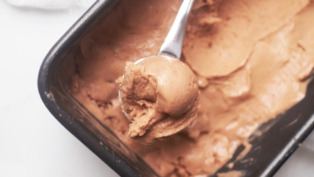 An ice cream scoop holds a scoop of chocolate nice cream.