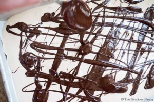 Drizzling melted chocolate over yogurt mixture on a cookie sheet.