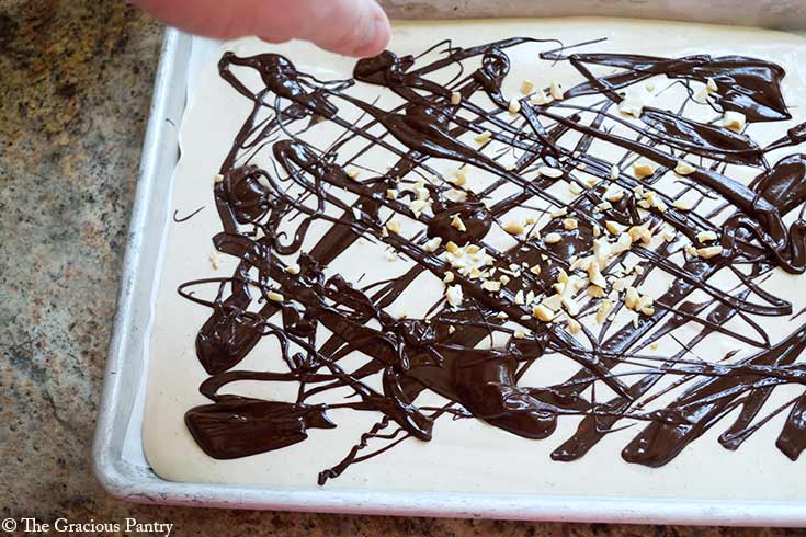 Sprinkling chopped peanuts over yogurt and chocolate on a sheet pan.