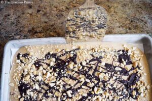 Loosening the frozen Chocolate Peanut Butter Frozen Yogurt Bark from the sides of the cookie sheet with a metal spatula.