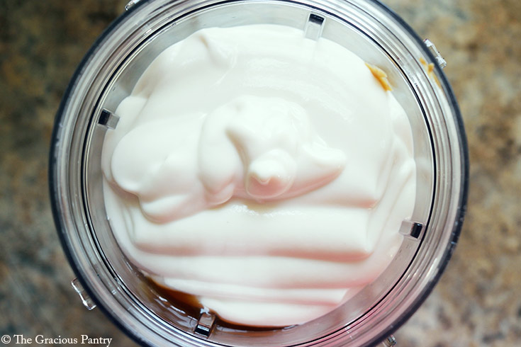 Yogurt in a blender tumbler with peanut butter and sweetener.