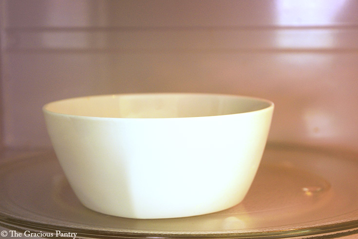 A white bowl of chocolate chips sitting in a microwave.