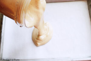 Pouring peanut butter yogurt mixture onto a parchment lined cookie sheet.