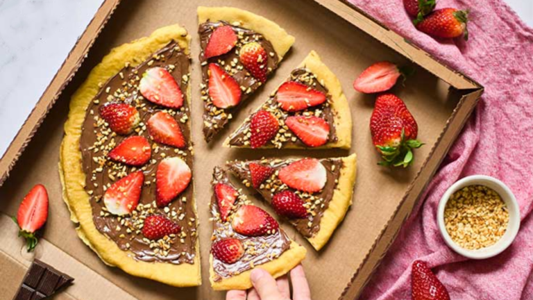 An overhead view of a chocolate pizza in a pizza box. A hand is reaching for one of the slices.