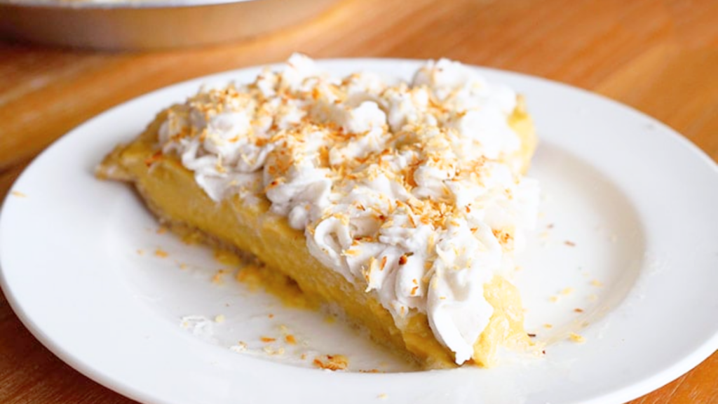 A slice of coconut cream pie sits on a white plate.