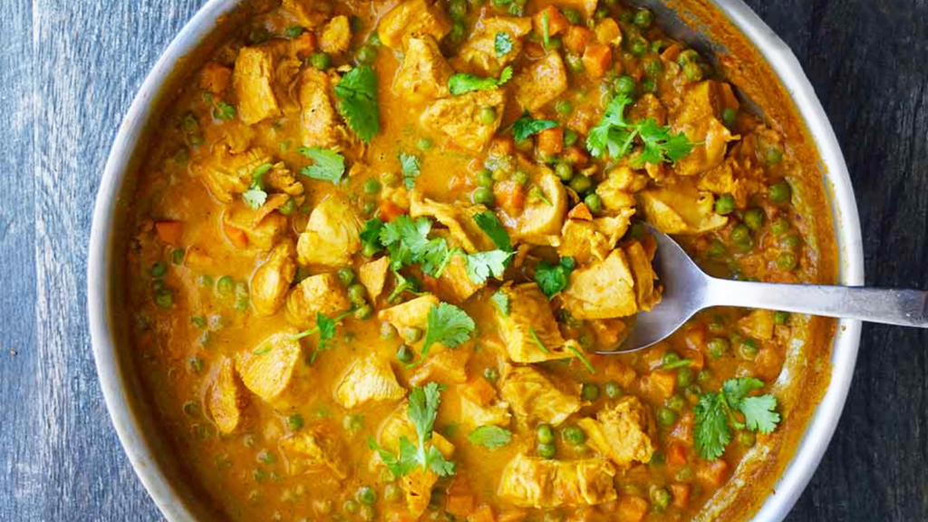 An overhead view of a skillet filled with coconut curry chicken. A metal spoon rests in the pan.