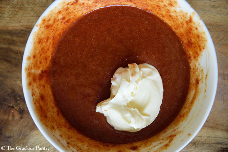 Mayo added to a bowl of sauce in a mixing bowl.