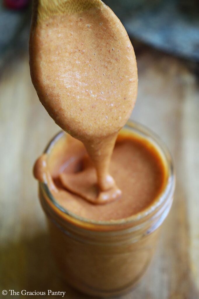 Copycat Chick-Fil-A Honey Roasted Barbecue Sauce drizzles off a wood spoon into a small canning jar filled with it.