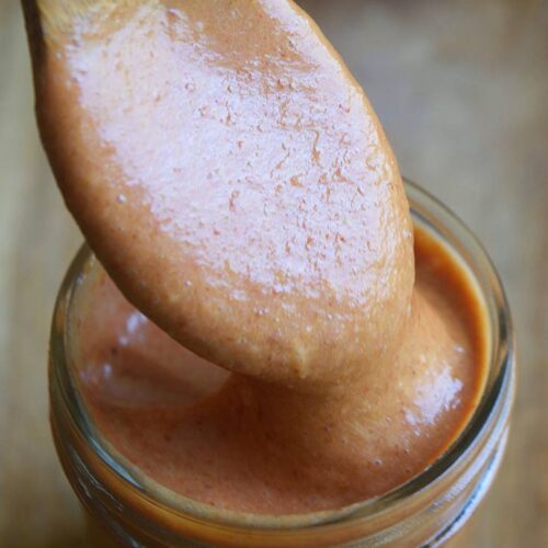 A wood spoon lifts some Copycat Chick Fil A Honey BBQ Sauce out of a canning jar that is full of the sauce.