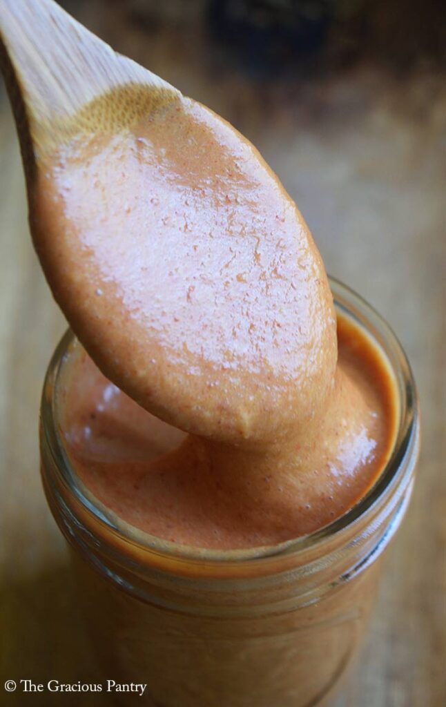 A wood spoon lifts some Copycat Chick-Fil-A Honey Roasted Barbecue Sauce out of a canning jar that is full of the sauce.