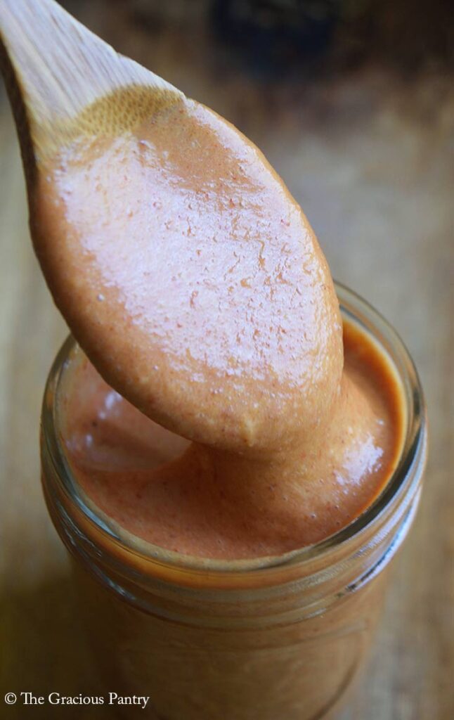 A wood spoon lifts some Copycat Chick Fil A Honey BBQ Sauce out of a canning jar that is full of the sauce.