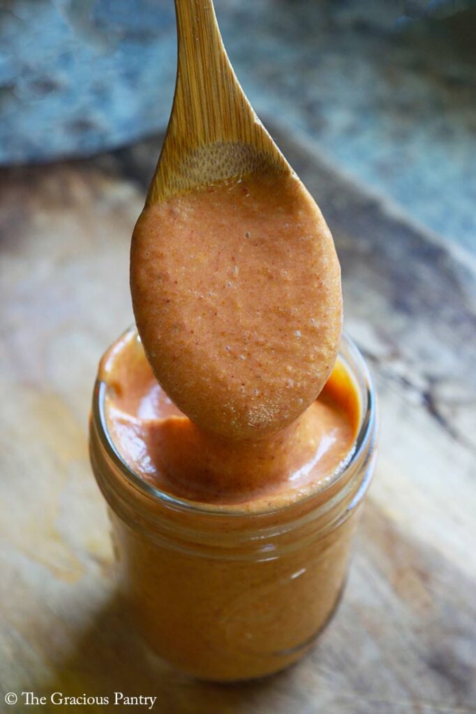 A front view of a wood spoon dripping sauce into an open canning jar.