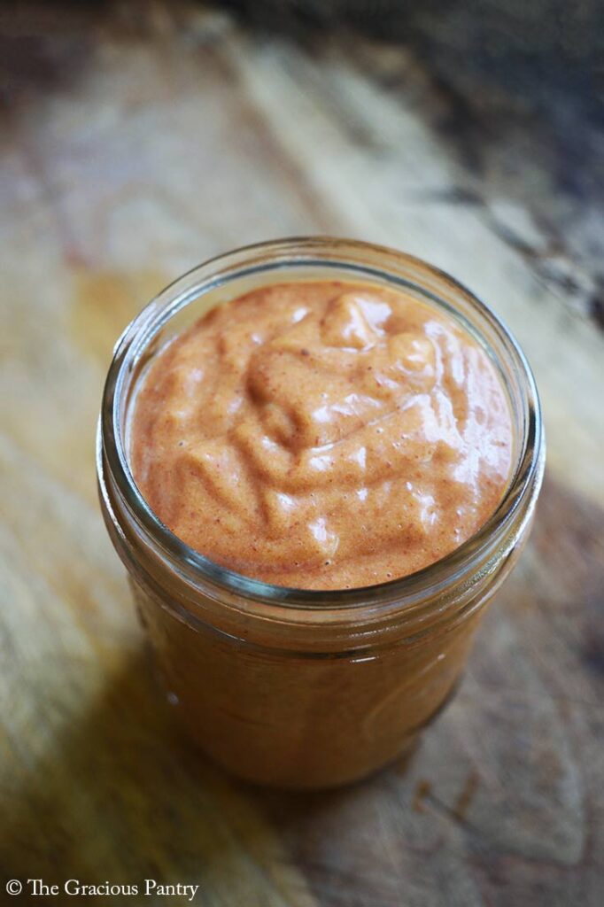 A canning jar sits on a wood surface, filled with Copycat Chick Fil A Honey BBQ Sauce.