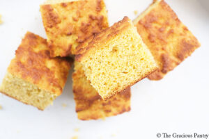 A pile of cut cornbread pieces lay on a white surface.