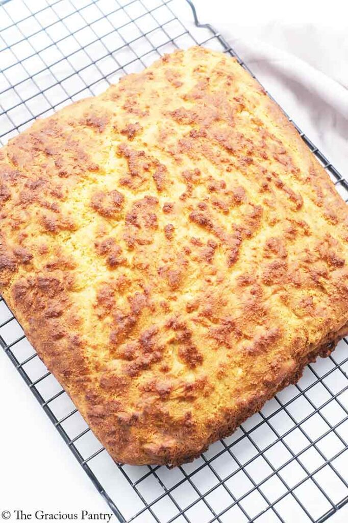 An uncut loaf of cornbread cooling on a black wire rack.