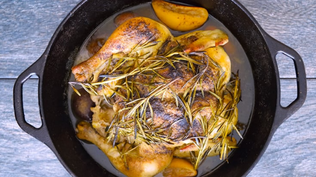 A dutch oven with a cooked whole chicken topped with rosemary twigs.