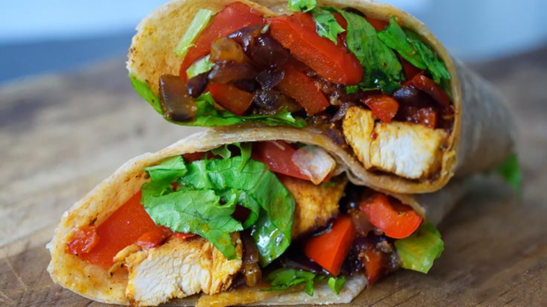 Two halves of a Fajita Wrap are stacked on top of each other on a wooden surface.