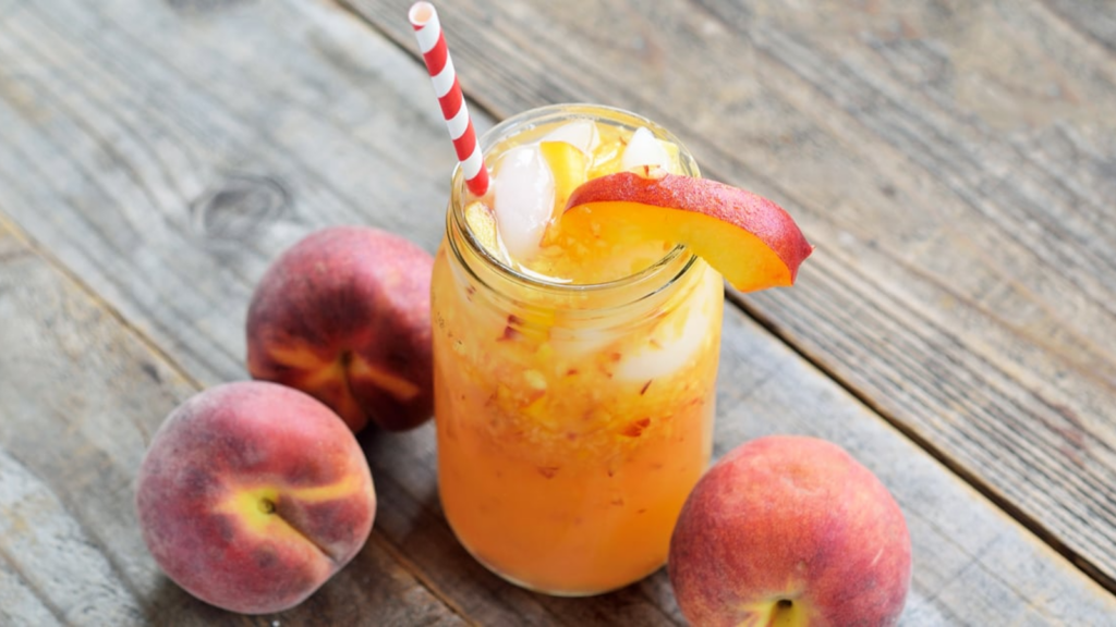 A glass jar filled with Georgia peach lemonade. It's garnished with a peach slice and a red and white stripped straw.