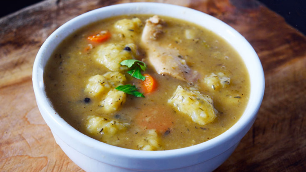 A white bowl sits on a wood surface and is filled with Germany potato dumpling soup.