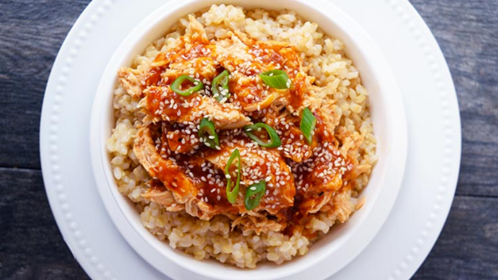 An overhead view of a white bowl filled with rice and topped with honey sesame chicken.