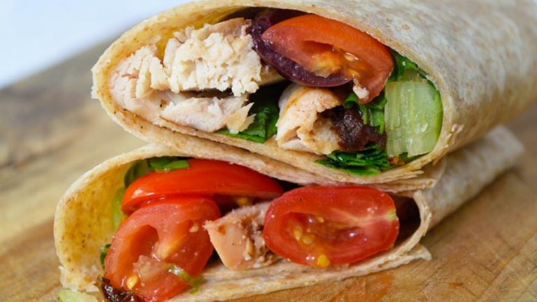 Two halves of an Italian Chicken Wrap are stacked on top of each other and are laying on a wood surface.