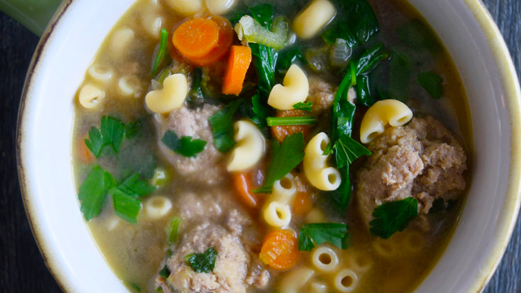 An overhead view of a light green crock filled with Italian wedding soup.
