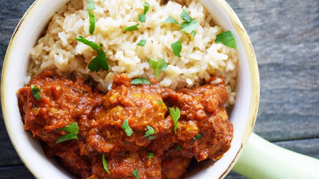 An overhead view of a light green crock holding kofta curry and rice.