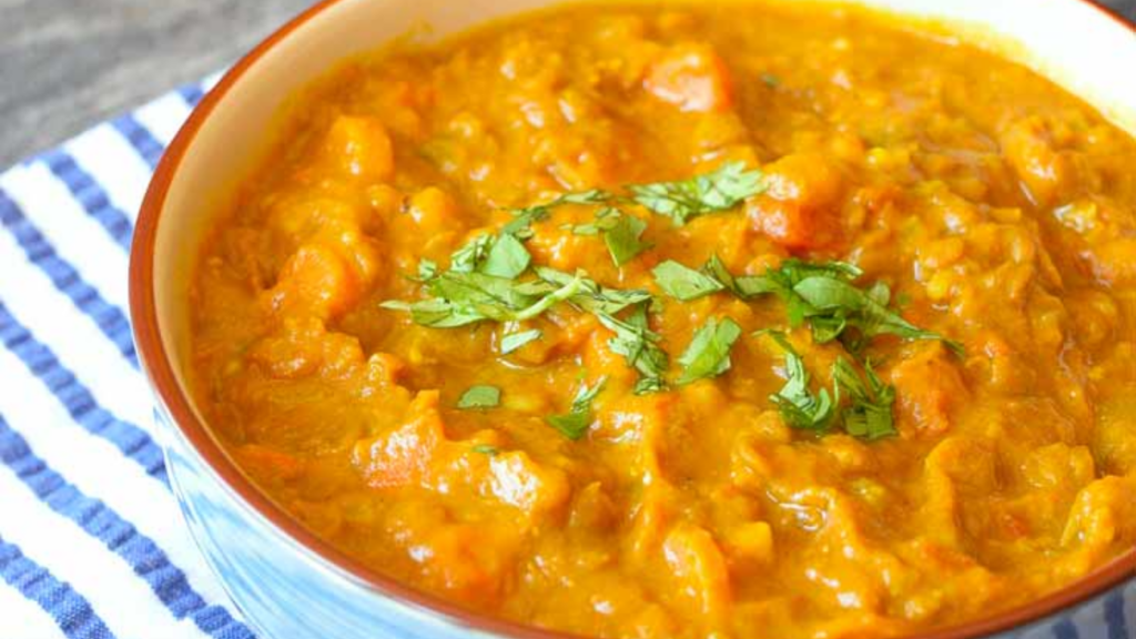 A blue bowl holds lentil curry and is garnished with fresh, chopped greens.