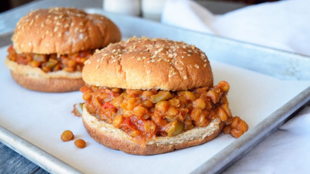 Two lentil sloppy joes sit on a parchment-lined baking pan.