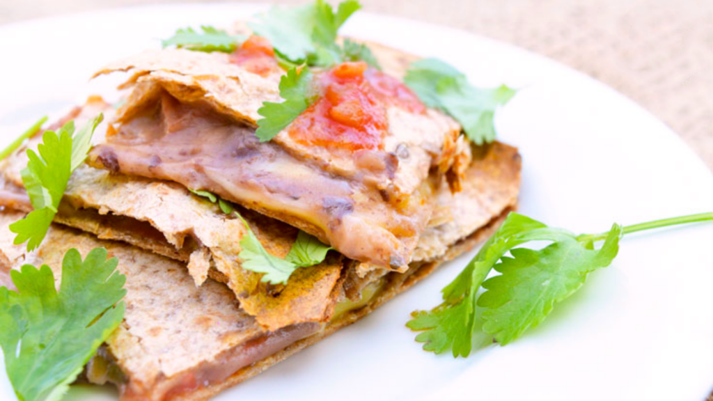 A portion of loaded sheet pan quesadilla sitting on a white plate, garnished with fresh cilantro.