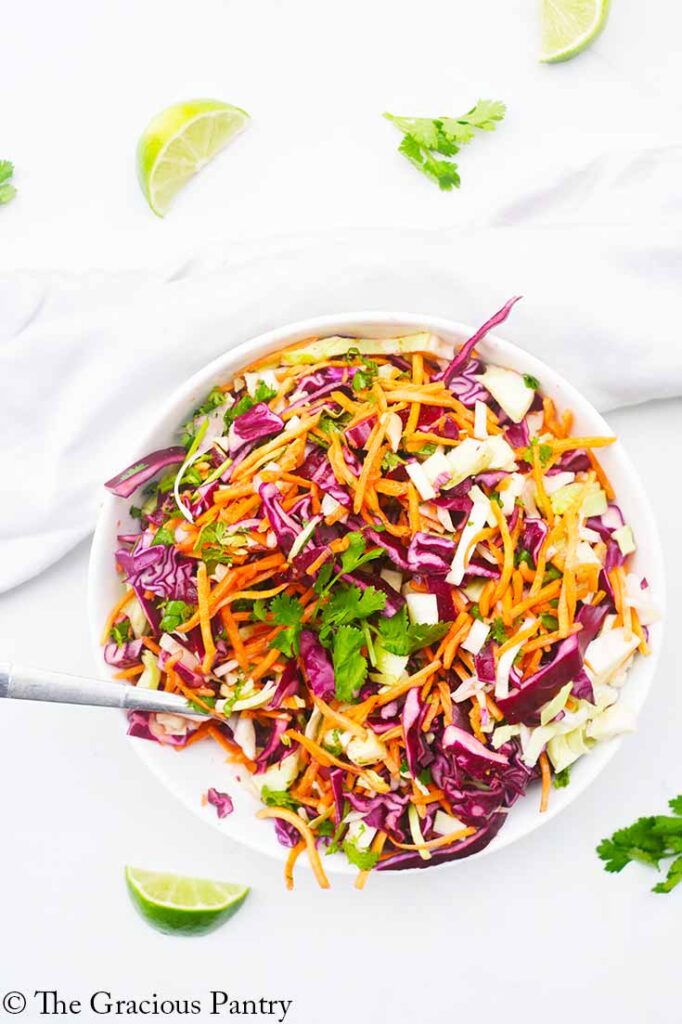 An overhead view looking down into a white bowl filled with Mexican Coleslaw. A fork rests on the side of the bowl.