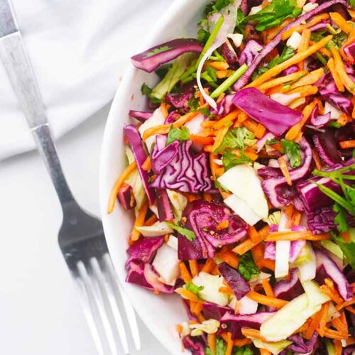 An overhead view looking down into a white bowl filled with Mexican Coleslaw. A fork lays to the side of the bowl.