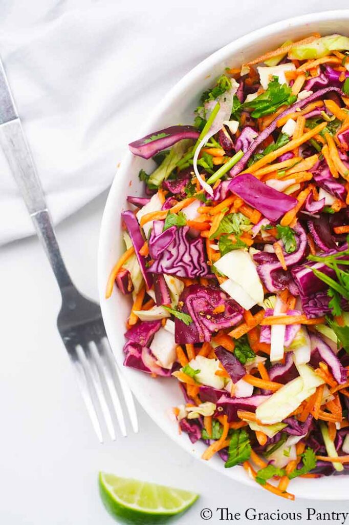 An overhead view looking down into a white bowl filled with Mexican Coleslaw. A fork lays to the side of the bowl.