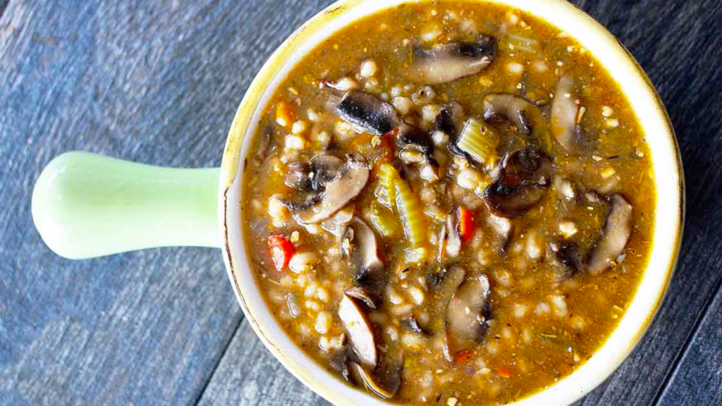 An overhead view of a light green crock filled with mushroom barley soup.