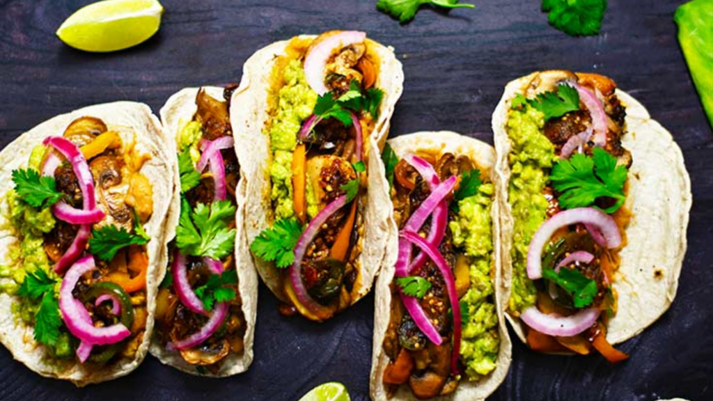 A row of mushroom tacos on a dark gray surface.